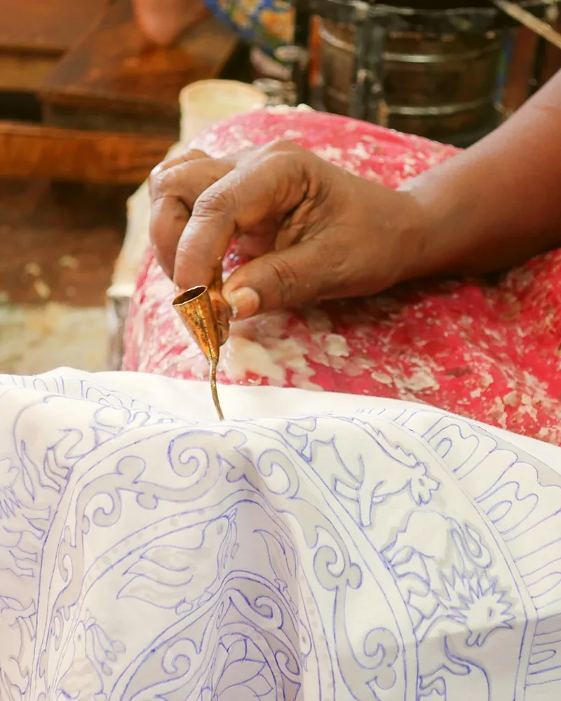 Canting con cera caliente trazando líneas finas sobre una tela blanca con dibujo previo